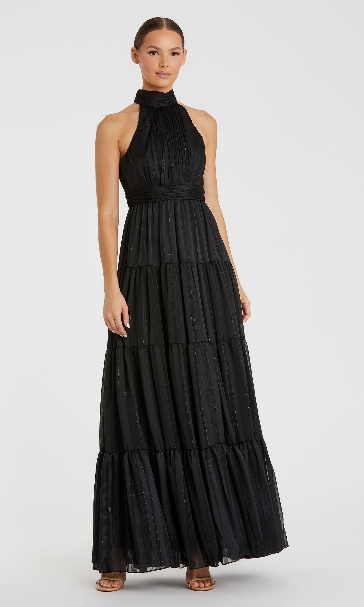 A woman wearing the Mac Duggal 49515 long black tiered formal dress with a high neck and sleeveless, floor-length design stands against a plain white background.